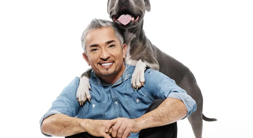 Cesar Millan z uśmiechniętym psem, który kładzie mu łapy na ramionach.